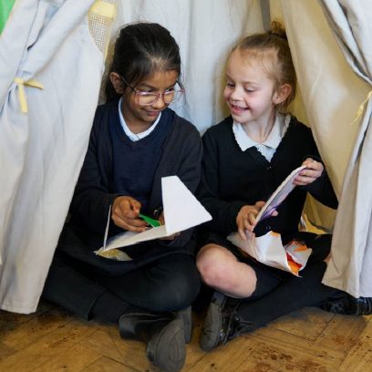 A vibrant promotional image for World Book Day featuring two children inside a makeshift tent, happily reading together. The text highlights "Our Impact 2025" and promotes a reading charity, with colorful stars and the National Book Tokens logo included.