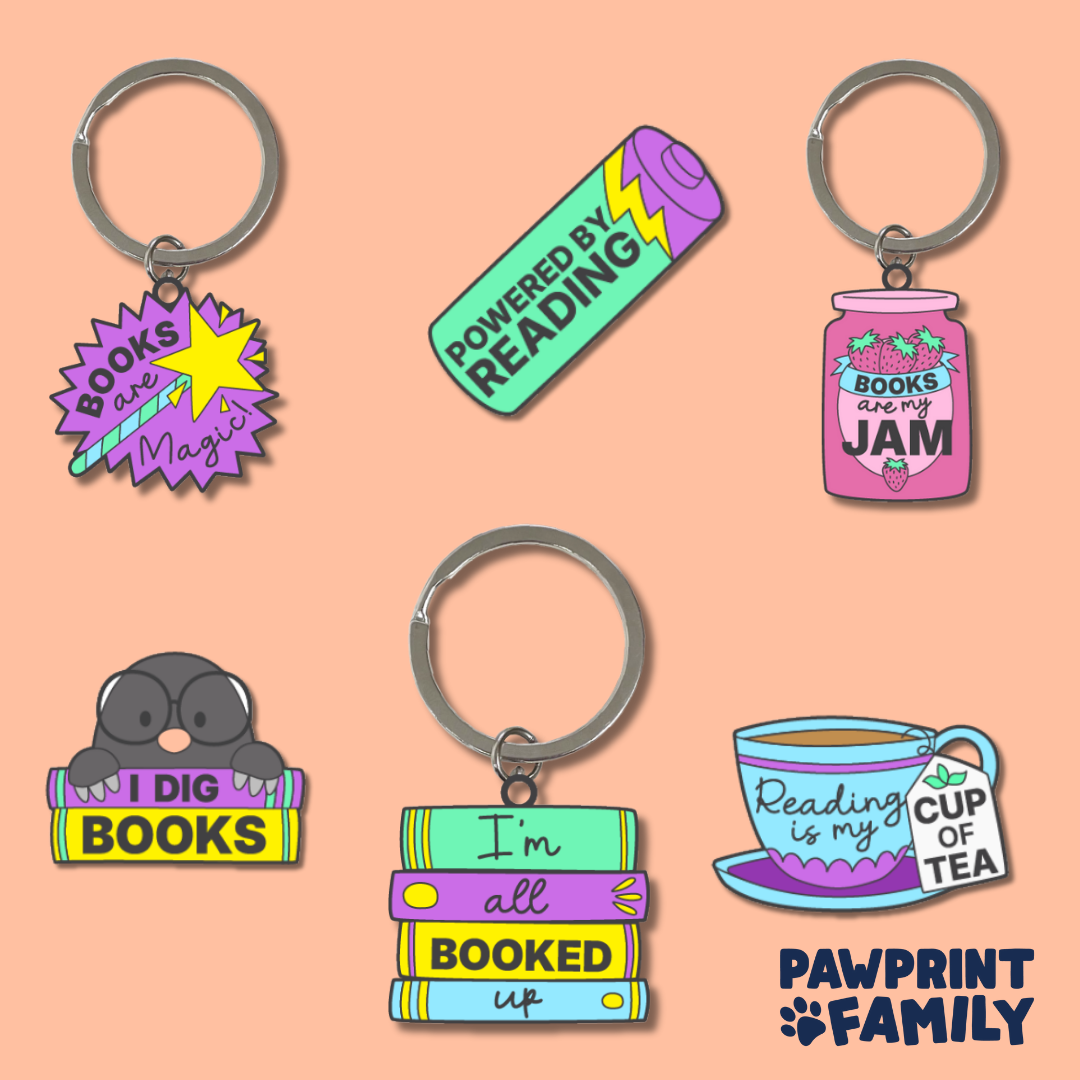 A collection of colourful keychains with book-themed designs and phrases like "Books are Magic," "Powered by Reading," and "I'm all booked up."