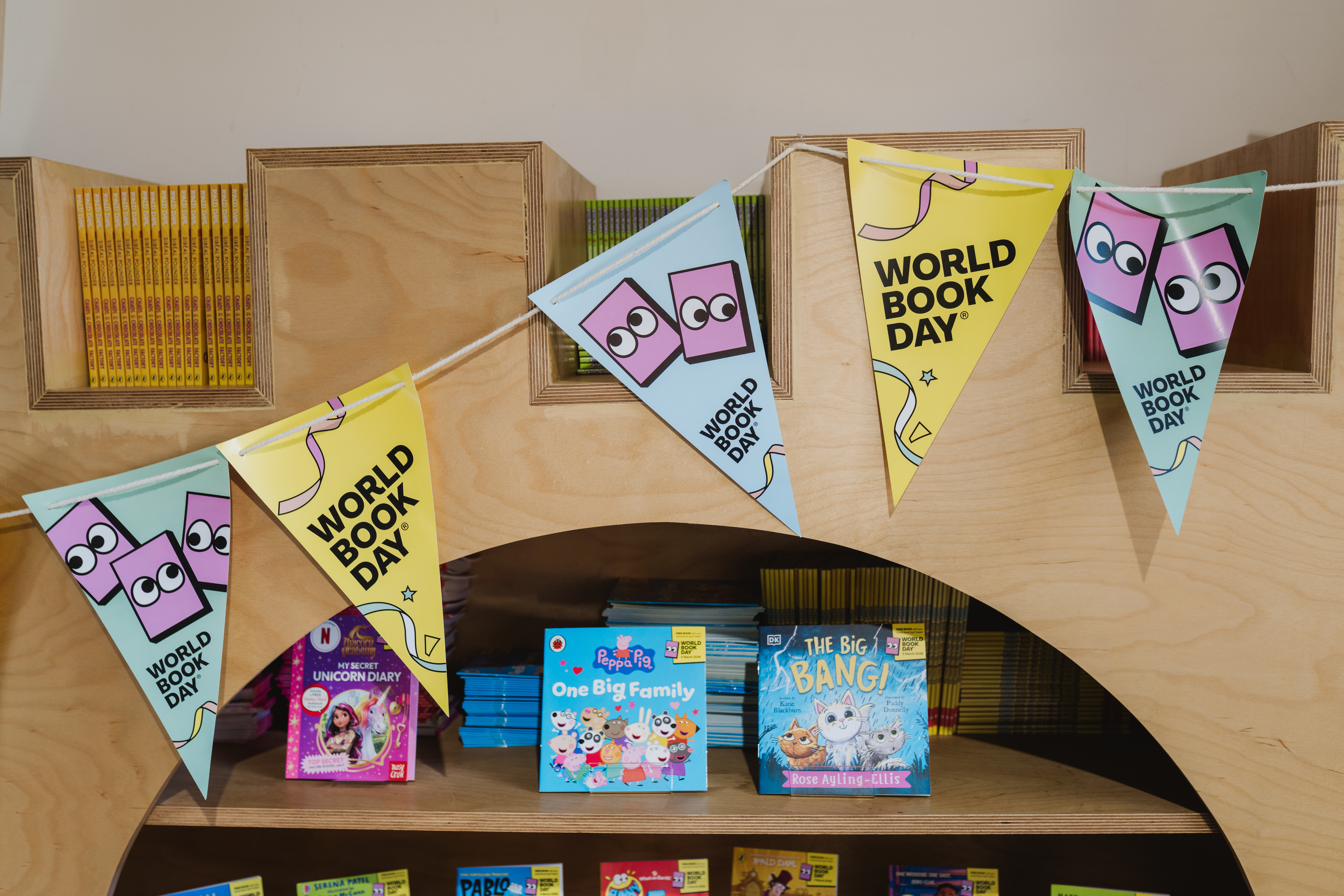 Bunting with "World Book Day" text hangs above a shelf displaying children's books, including "Unicorn Diary," "One Big Family," and "The Big Bang."