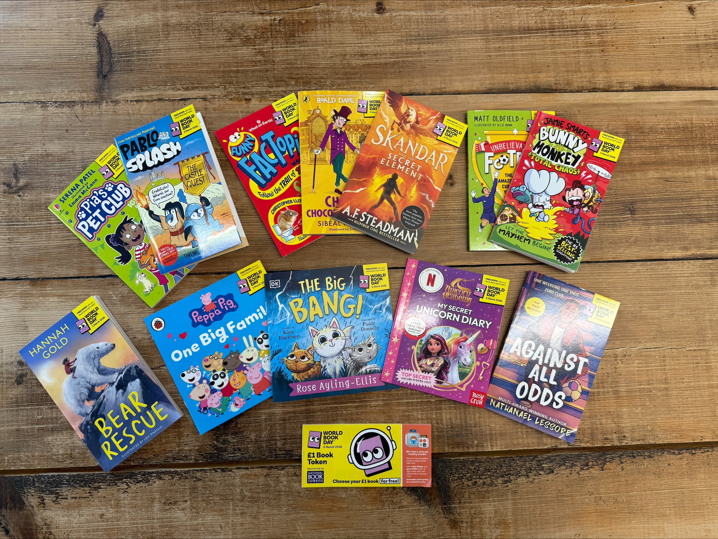 A collection of children's books featuring vibrant covers displayed on a wooden surface, accompanied by a £1 book token. Titles include stories about animals, fantasy adventures, and family tales, part of a World Book Day selection.